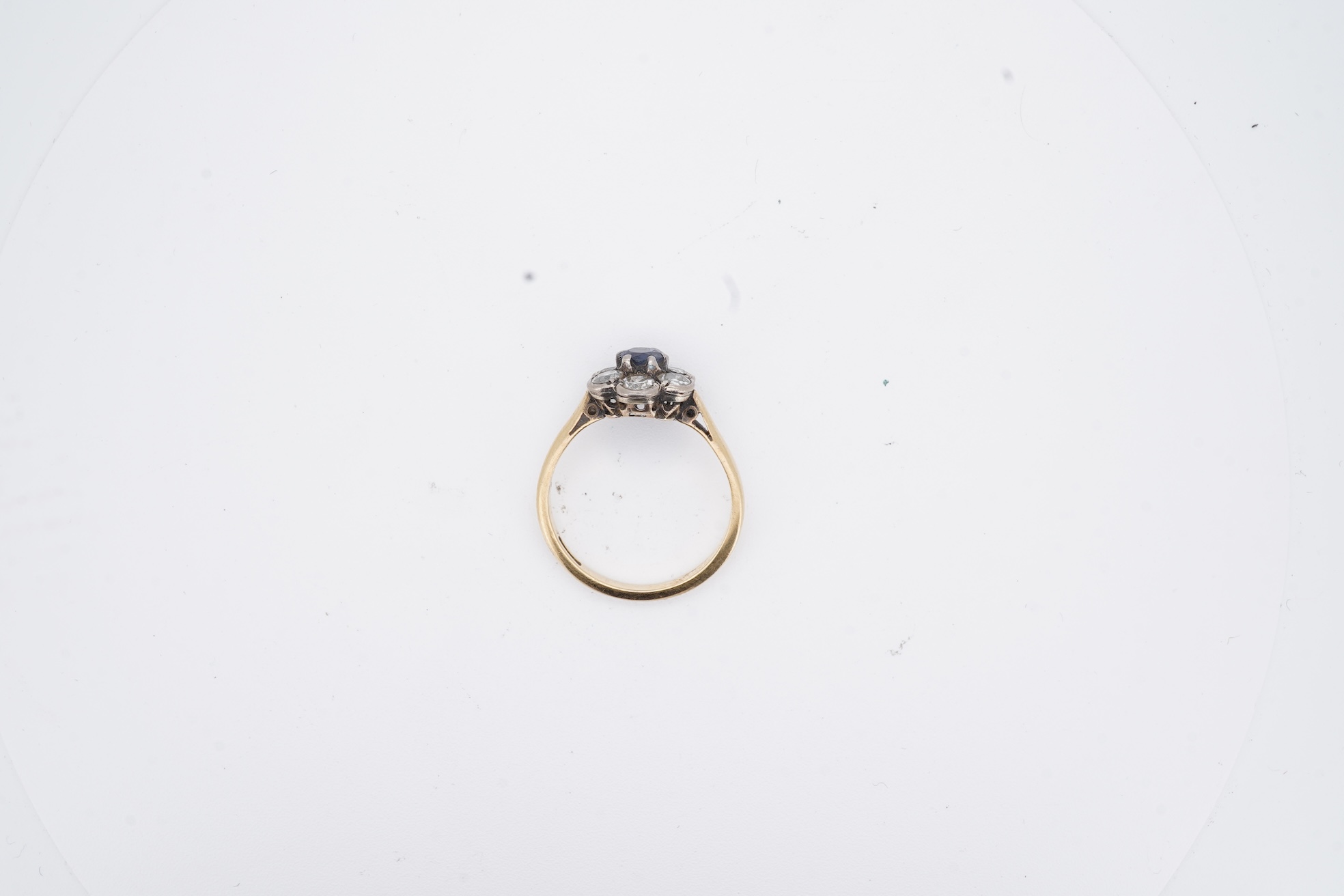An early to mid 20th century yellow metal (stamped 18ct), singe stone sapphire and six stone diamond set circular cluster ring, size O, gross weight 3.7 grams.